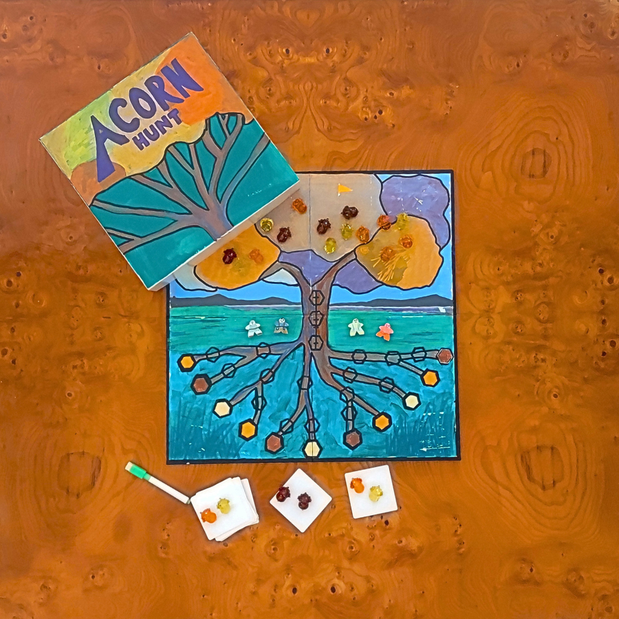 A children's board game set titled 'Acorn Hunt' arranged on a textured orange-brown wood surface. The set includes a colorful game board featuring a stylized tree with acorns, a matching game box, three small white cards, and a green-handled tool.