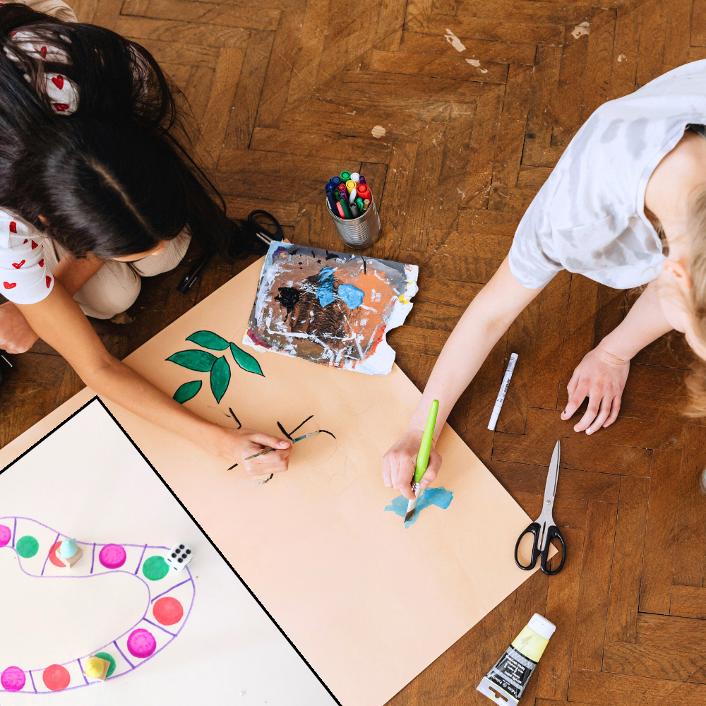Two children engaged in a game making activity on a wooden floor.